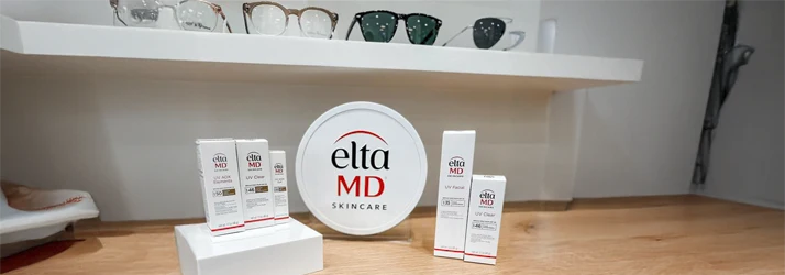 EltaMD skincare products showcased on a wooden counter beneath shelves of stylish eyewear.