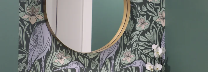 Decorative nook with patterned wallpaper, a round mirror, and a marble accent shelf.