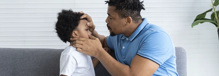 Father checking his sons eye on couch